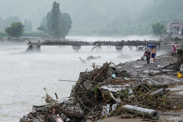 Orang-orang berjalan melewati jembatan yang rusak setelah hujan deras membanjiri area tersebut, di distrik Huairou, Beijing, China, Senin (28/7/2025). Foto: Stringer/REUTERS