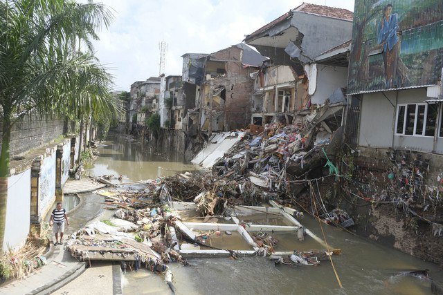 Warga berjalan di pinggir sungai yang berdekatan dengan bangunan toko dan rumah yang amblas akibat banjir di Denpasar, Bali, Kamis (11/9/2025). Foto: Nyoman Hendra Wibowo/ANTARA FOTO